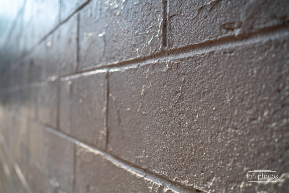 A brick wall painted white with many layers of paint, some peeling.