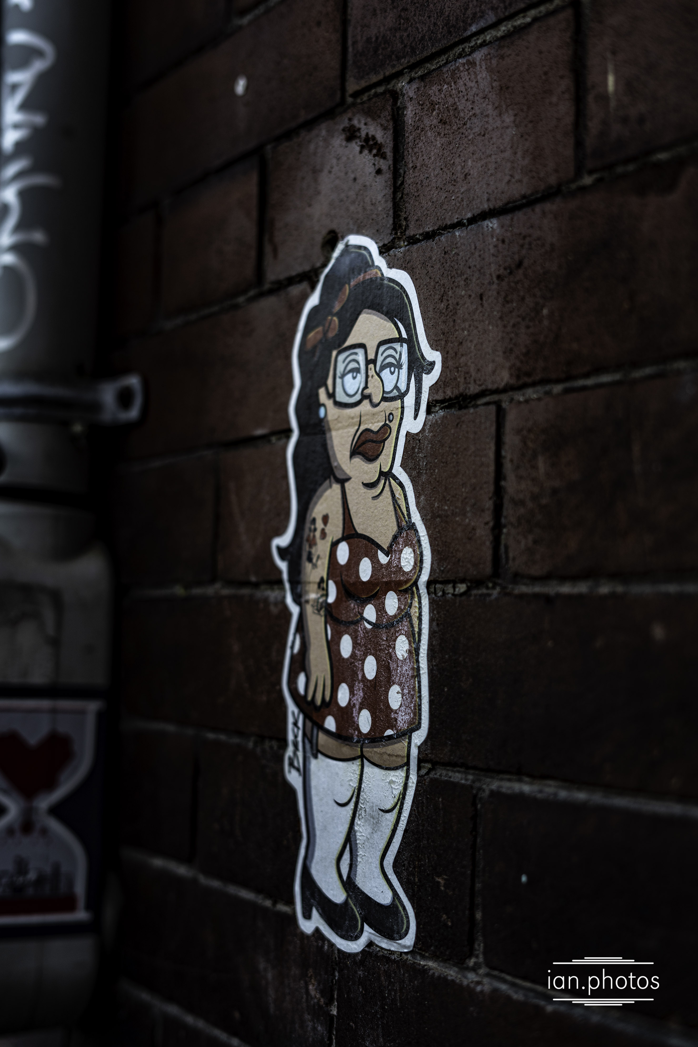 Sticker of a woman in the style of seth macfarlane on a brick wall in cabbage town.