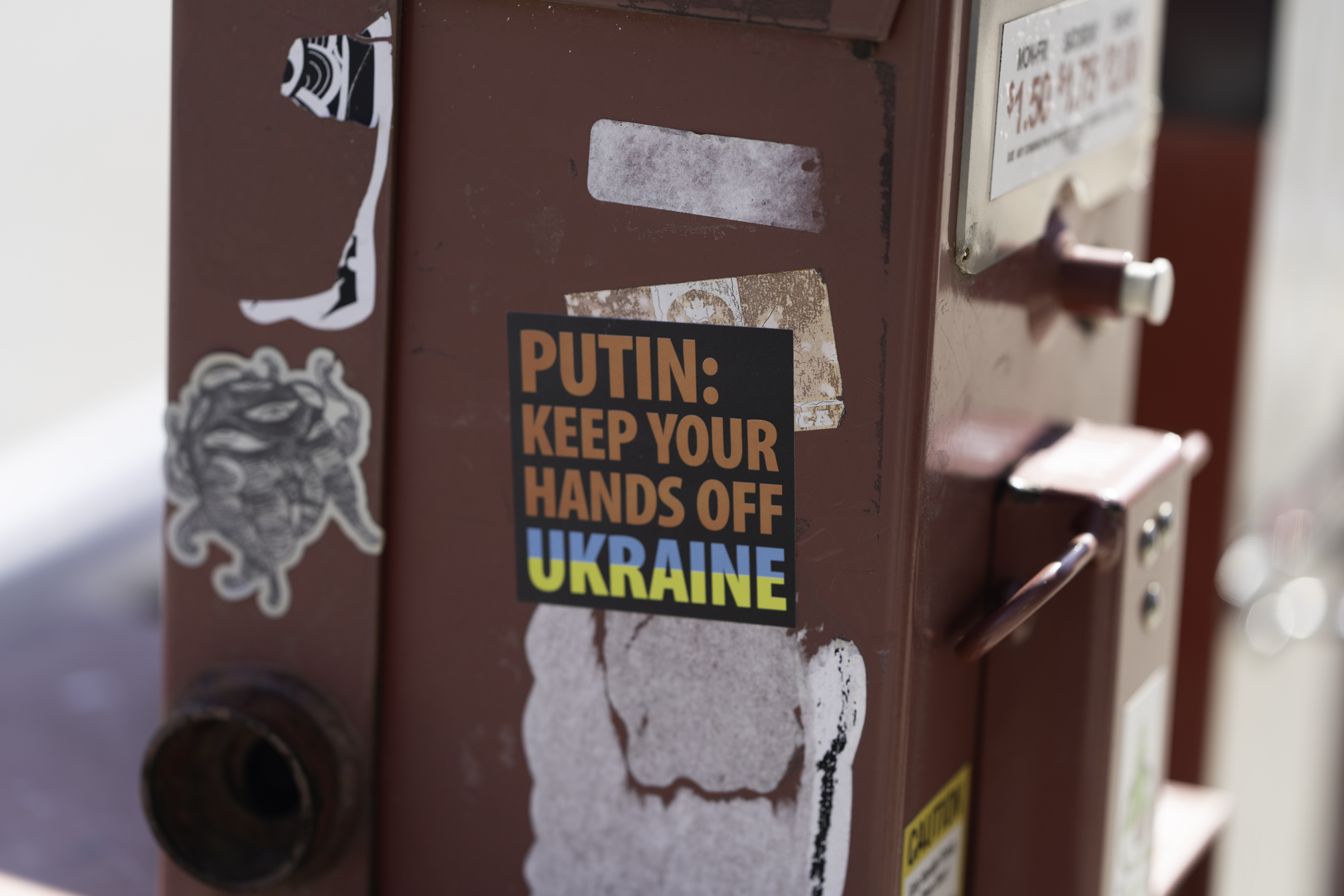 red newsboy with a black sticker in orange text "PUTIN: KEEP YOUR HANDS OFF UKRAINE" and UKRAINE IS STYLED LIKE THE UKRAINIAN FLAG. 