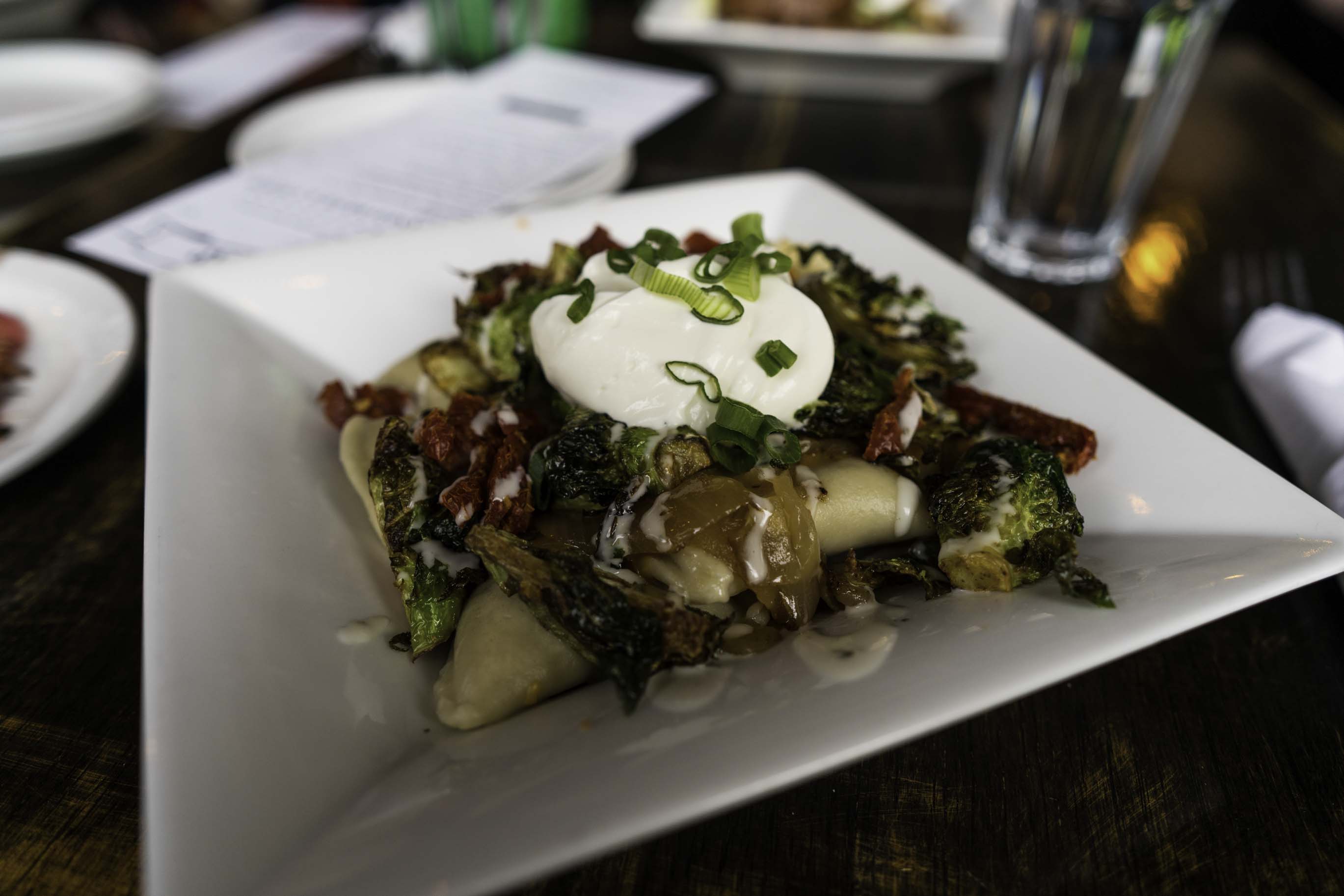 Picture of a plate of pierogis, covered in sour cream and cabbage.