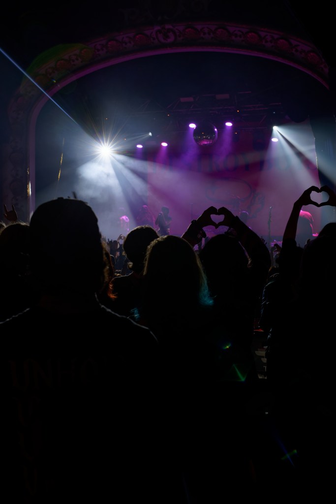 The crowd is going wild the lights shine into the camera and many fans have made hearts with their hands. 